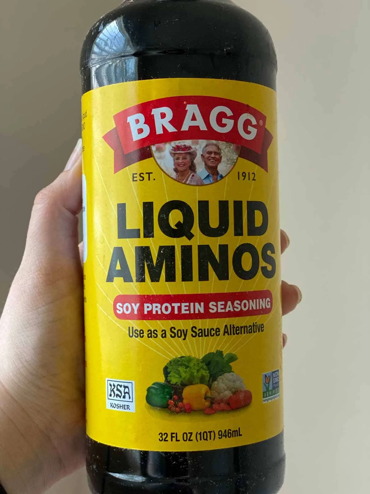 holding bottle of Bragg Liquid Aminos