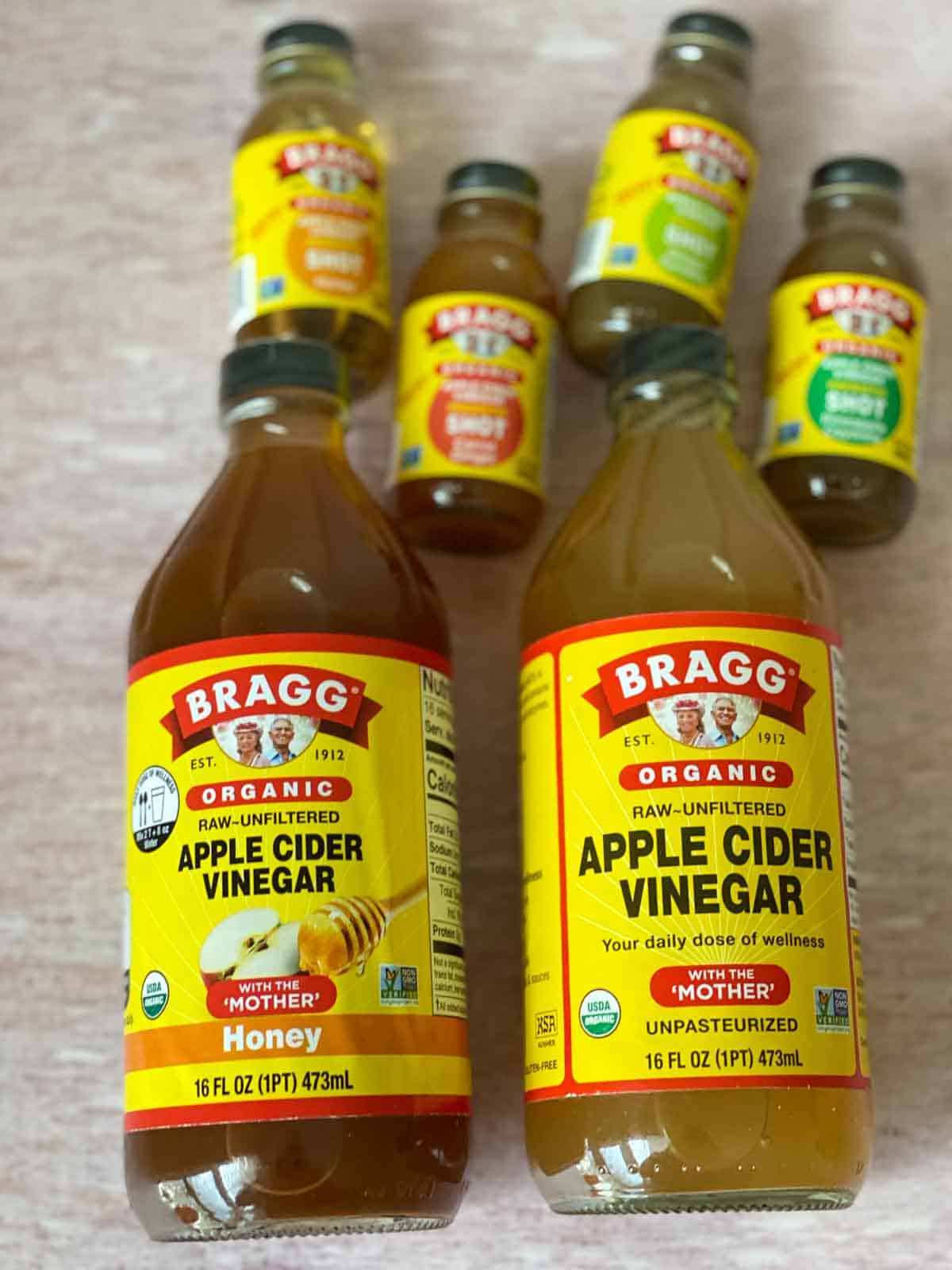 Bragg apple cider vinegar - 4 mini shot bottles laying above 2 large bottles