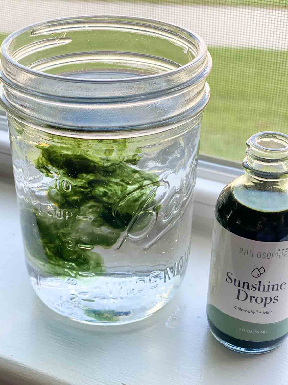 a glass of water with sunshine drops next to drop bottle