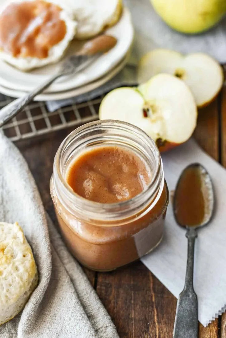 Small Batch Stovetop Apple Butter in jar with spoon and slices of apples next to it.
