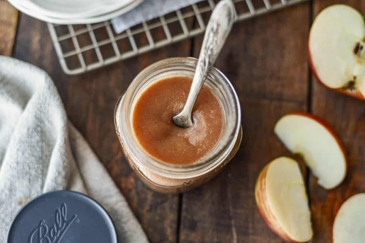 Small Batch Stovetop Apple Butter in jar with spoon and slices of apples next to it.