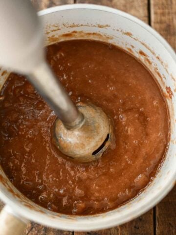 immersion blender in pot of apple butter making the texture smooth.