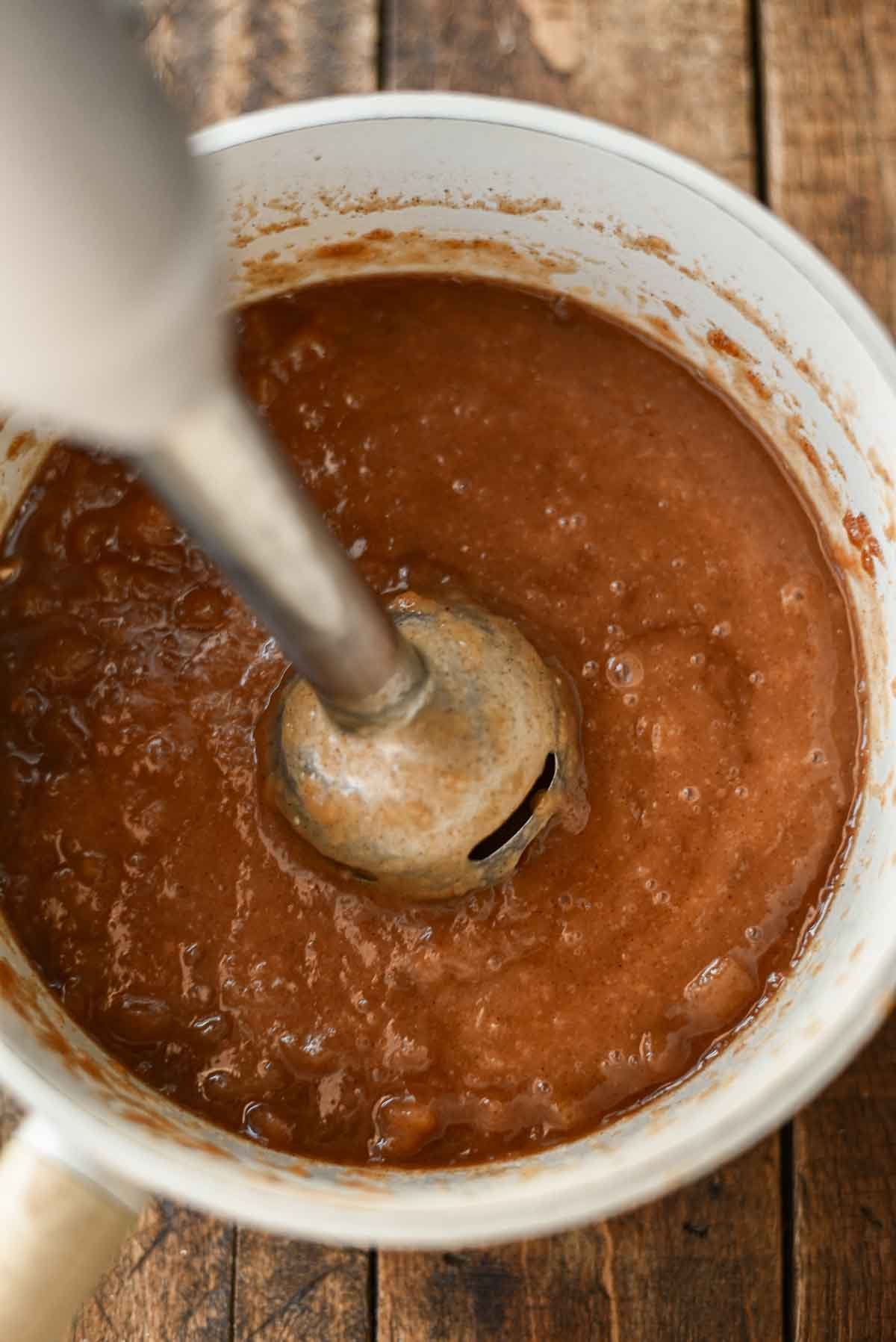 immersion blender in pot of apple butter making the texture smooth.